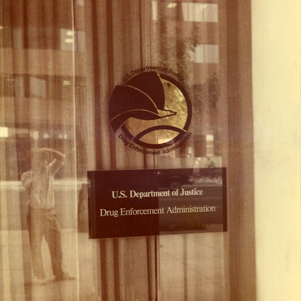 Rick Doblin captures himself in the window of a DEA office, 1984.